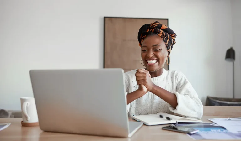 young woman cheering while working on a laptop at home