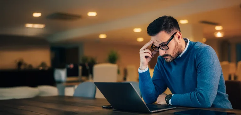 Focused adult male boss reading an e-mail over the laptop, sitting at the workplace.