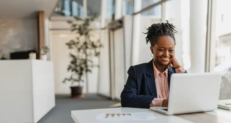 Smiling businesswoman working on a laptop in a modern, well-lit office.