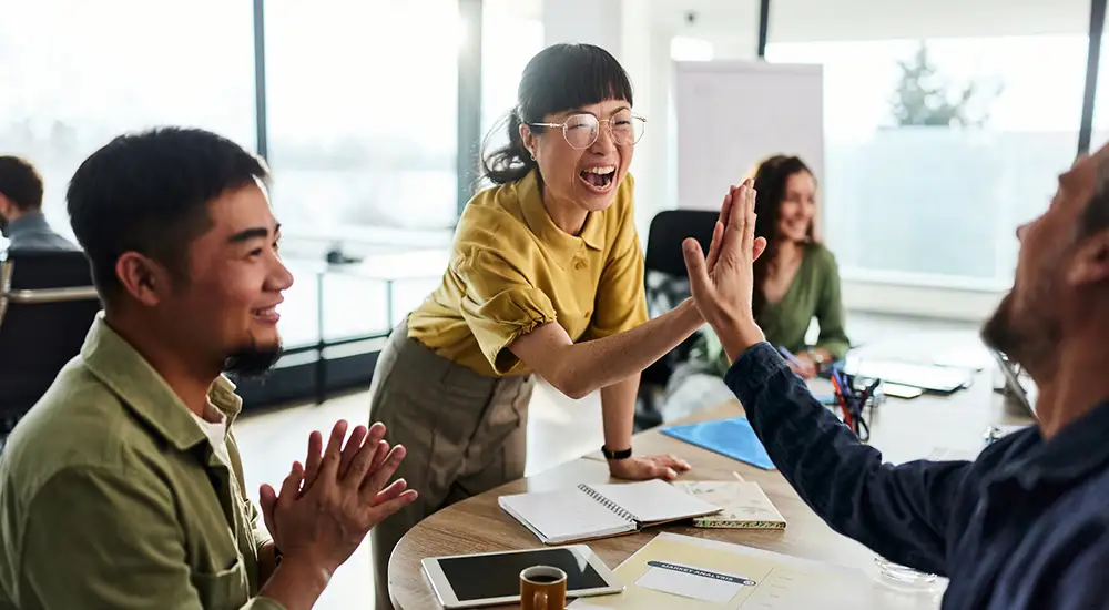 ServiceNow--Yokohama-release-2147499455 Cheerful Japanese businesswoman giving high-five to her male colleague during a casual meeting in the office.