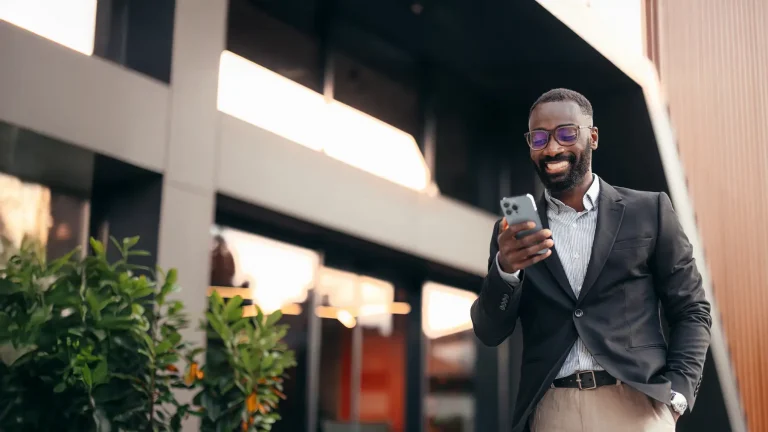 Businessman reading a message on his mobile phone while walking in front of the business building